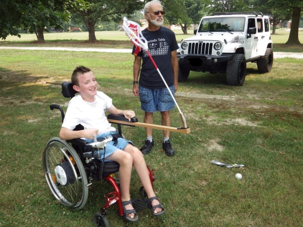 Caleb in a wheelchair with an attached lacrosse stick engineered to allow him to play.