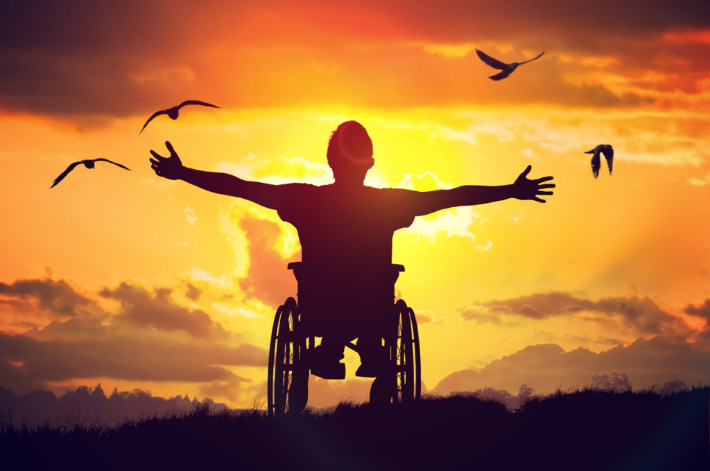 Disabled man has a hope. He is sitting on wheelchair and stretching hands at sunset.