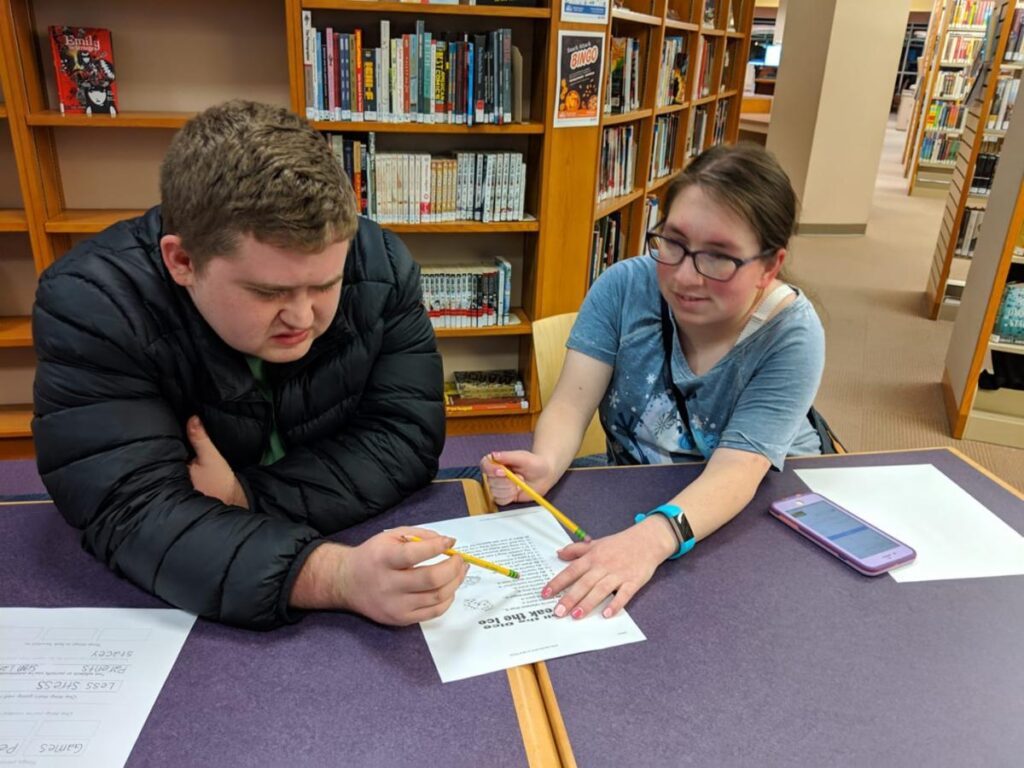 A female Peer Mentor student assisting another male student in a learning activity with pencil and paper at a Connect program event. 