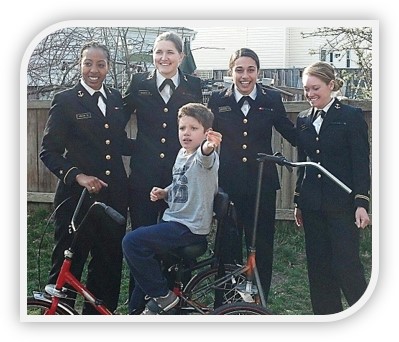 Colby on his new custom tricycle with four women engineering students in their Navy uniforms.