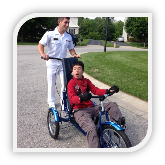 Engineering student in white naval uniform behind Kevin on his custom bicycle.