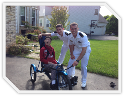 Two engineering student in white naval uniforms with Kevin on his custom bicycle.
