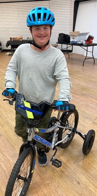 Boy in bike helmet pushing a modified bicycle.