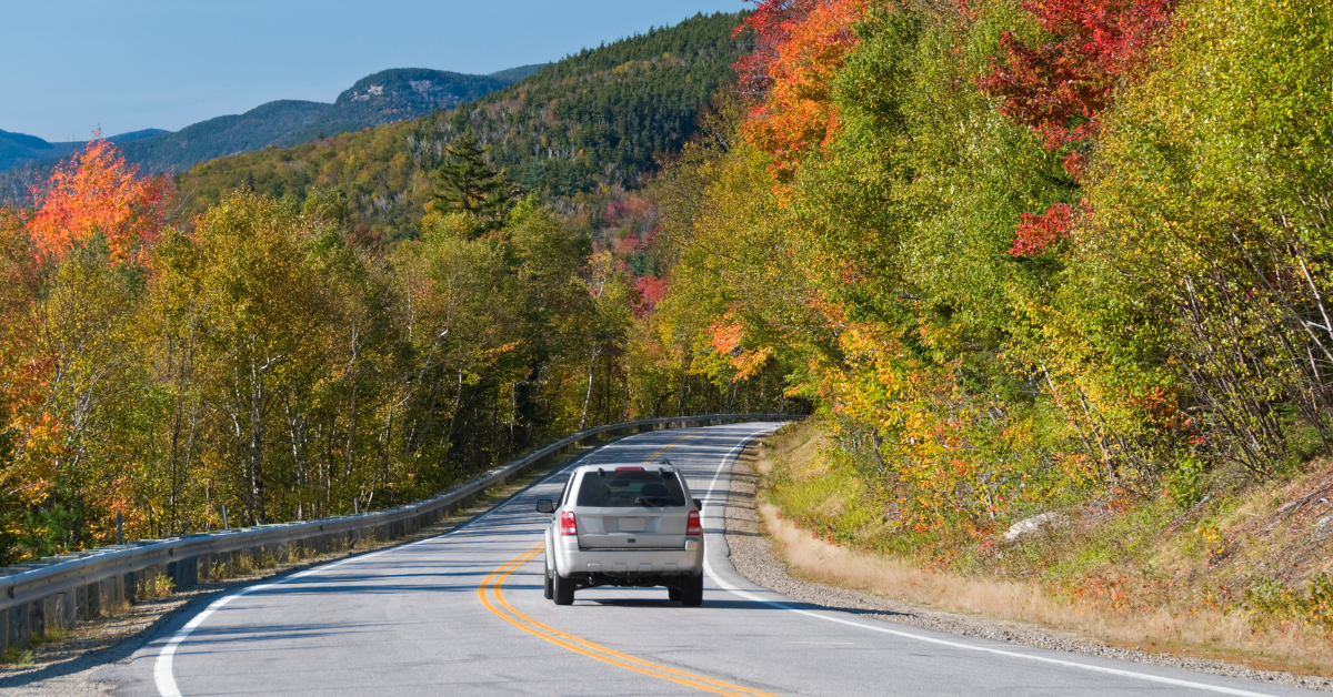 A car on an open highway surrounded by fall foliage.