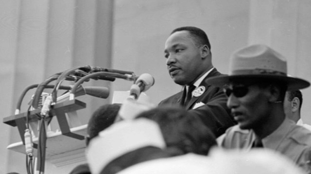 Black and white photo of Dr. Martin Luther King Jr. at a podium and park ranger in the foreground.