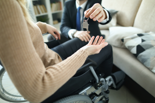 Agent Hands over Keys with a house-shaped keychain to a Person in a Wheelchair.