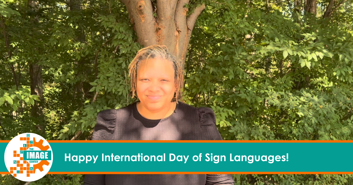 Usherla DeBerry is a Black woman with light brown braided hair. She wears a black blouse and stands outdoors in front of a leafy tree while communicating the above message using American Sign Language (ASL)