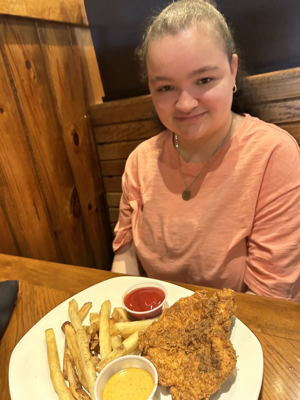 Ally Sloat smiling at a restaurant table with a plate of fries and fried chicken in front of her.