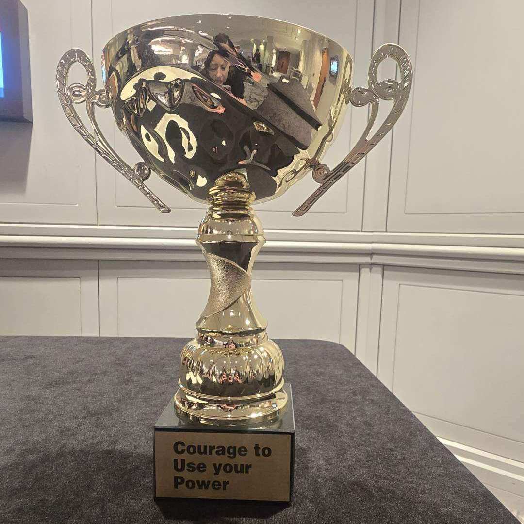 A large gold trophy with handles on each side and the engraved words “Courage to Use your Power” on the base.