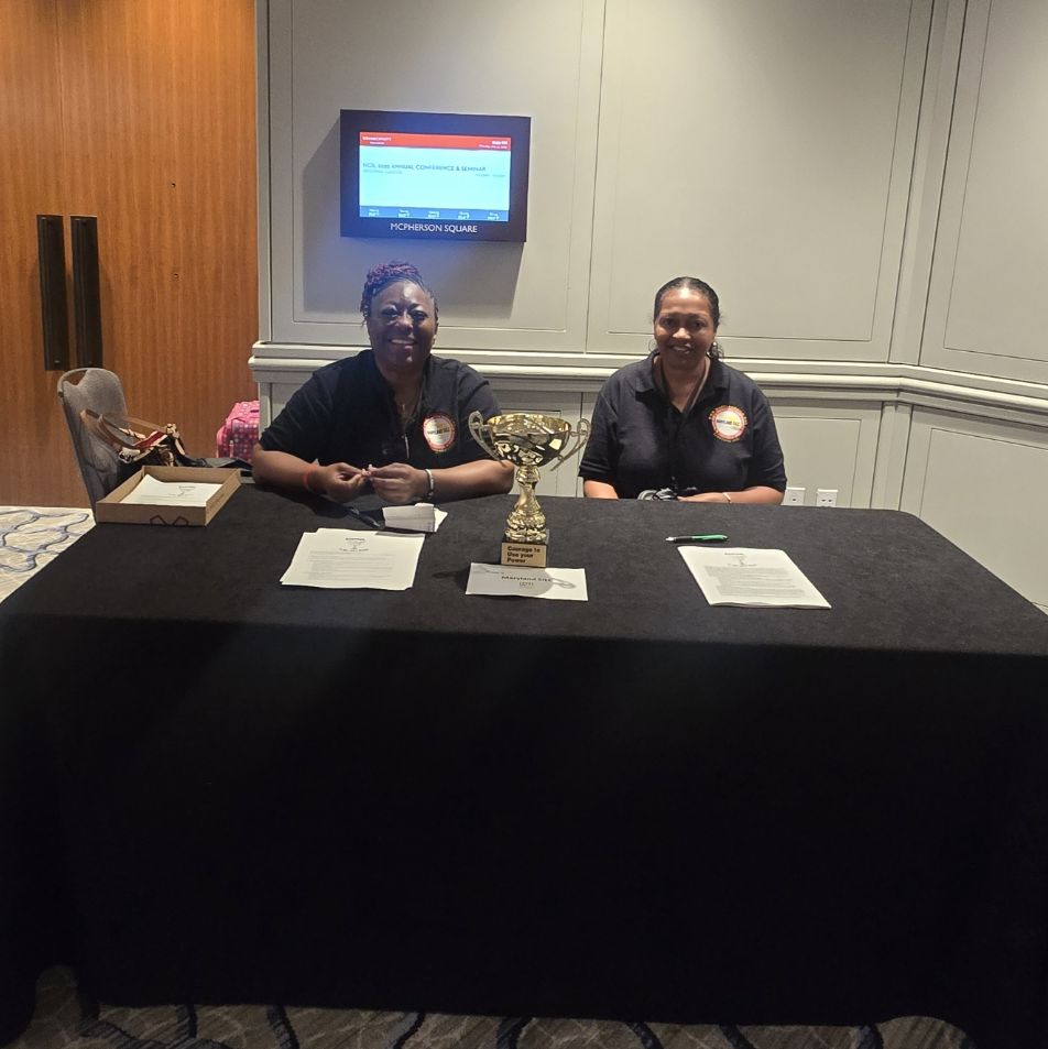 Lorna-Mae Silcott and another Maryland SILC representatives sit at an exhibit table with the CUP trophy and informational materials displayed.
